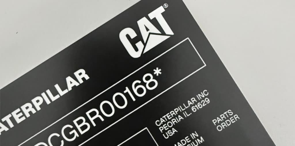 Czarna tabliczka znamionowa Caterpillar z numerem identyfikacyjnym i polami danych