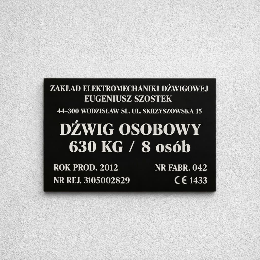 Czarna tabliczka opisowa dźwigu osobowego z nazwą producenta, udźwigiem i znakiem CE