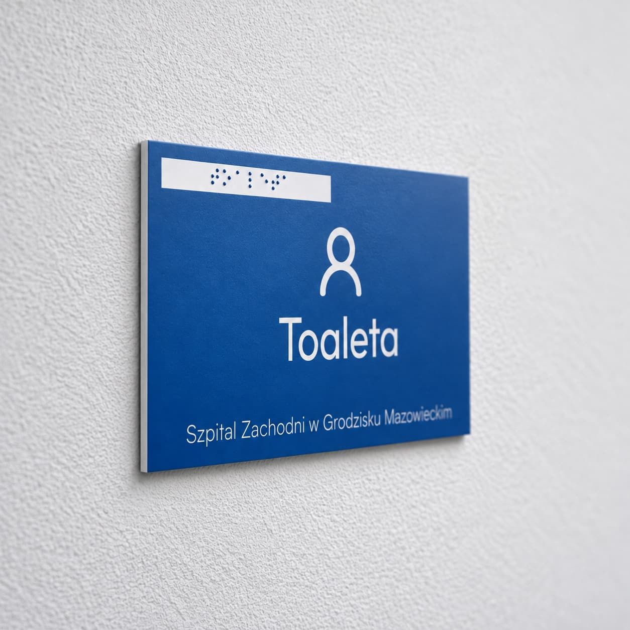 Niebieska tabliczka na drzwi gabinetu z piktogramem, zapisem Braille’a i białym grawerem