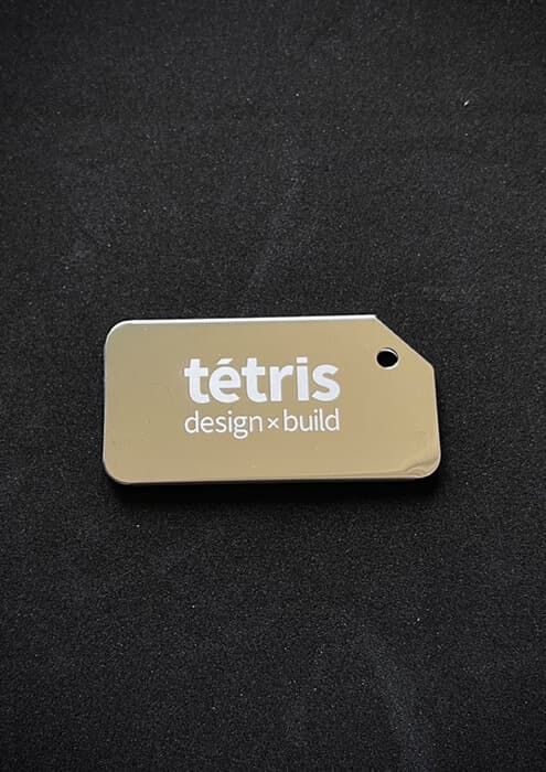 Mała stalowa plakietka z wykonanym znakowaniem laserowym logo tétris design x build.