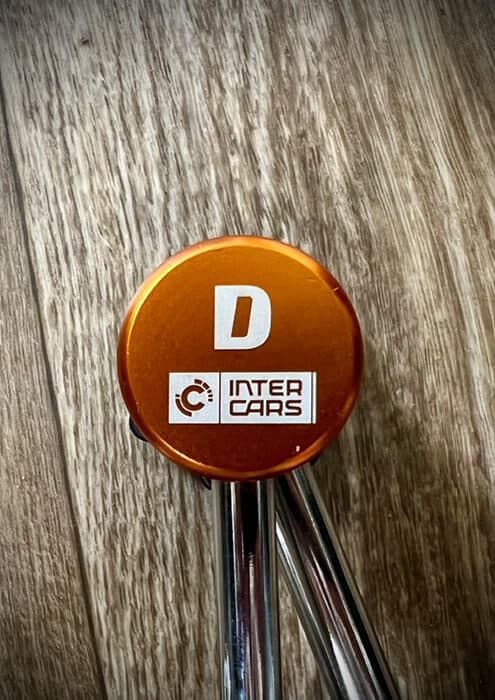 Znakowanie laserowe na pomarańczowym aluminiowym elemencie technicznym z logo Inter Cars.